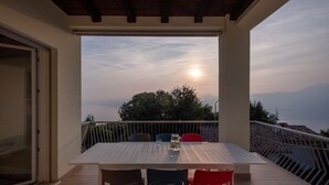 A balcony with a table and chairs, overlooking a scenic view of the sea and mountains.