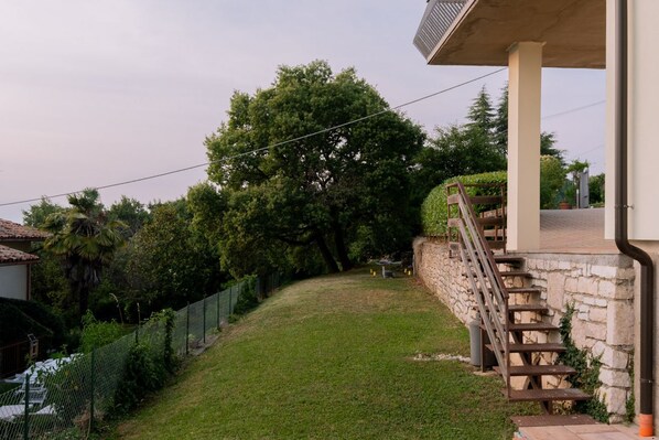 Un patio cubierto de césped con un muro de piedra, una escalera de madera y una valla de metal.