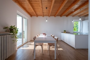 A modern kitchen with a wooden ceiling, a dining table with chairs, and a view of greenery outside.