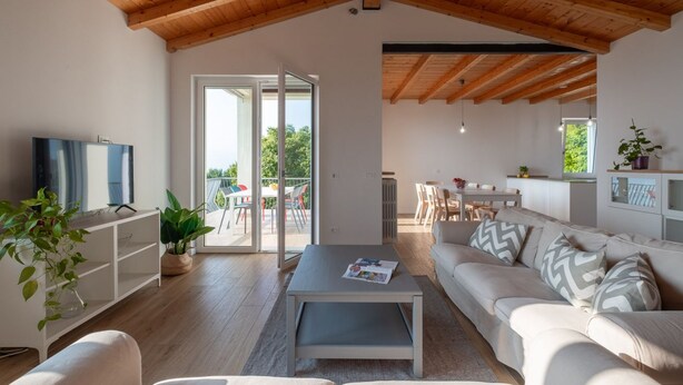 A modern living room with a wooden ceiling, a sofa, a coffee table, and a TV on a white cabinet.