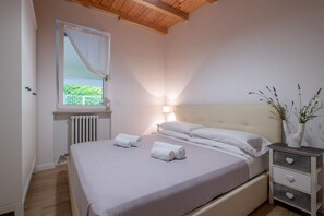 Ein Schlafzimmer mit Bett, Nachttisch, Fenster mit Vorhängen, Heizkörper und Lampe.