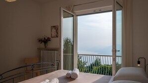 A bedroom with a bed, a chair, a radiator, a vase with flowers, and a balcony with a view.