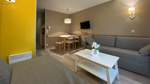 Una sala de estar moderna con un sofá, una mesa de centro, un comedor con sillas y un televisor montado en la pared.
