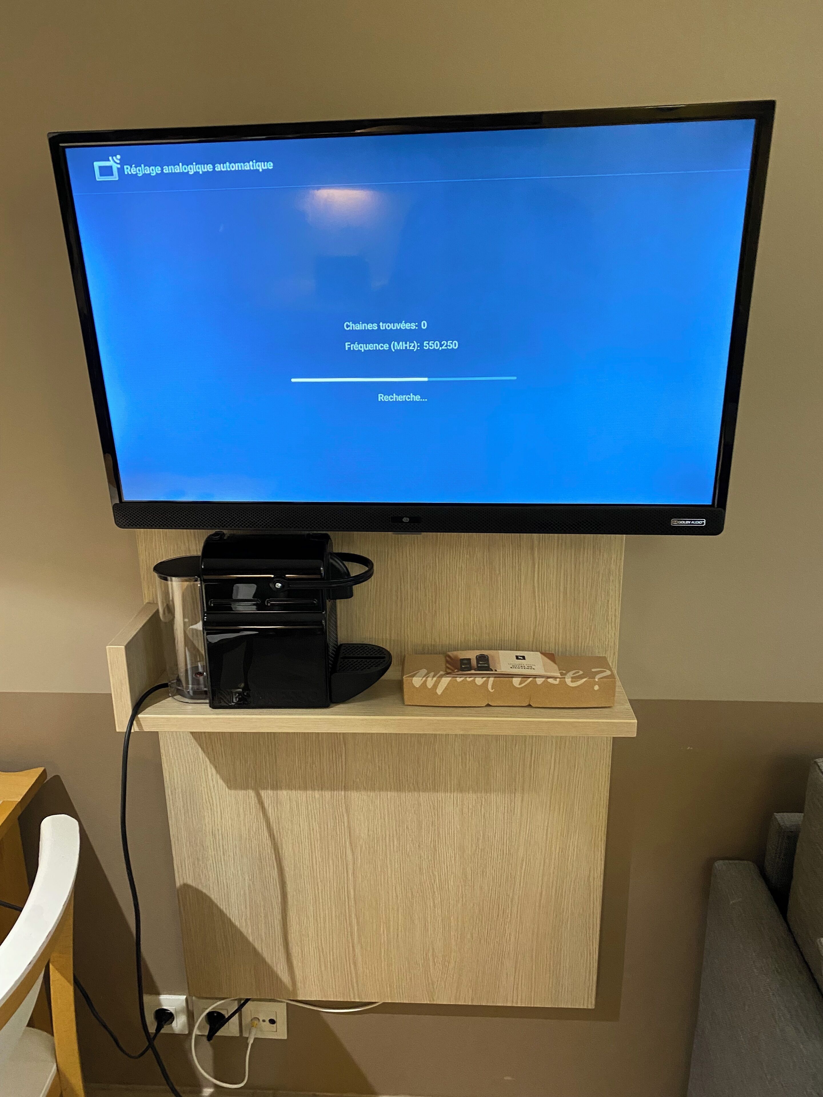 A flat-screen TV mounted on a wooden cabinet with a coffee machine and a box on it.