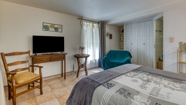 Un dormitorio con una cama, televisión, una silla, una mesita y un armario.