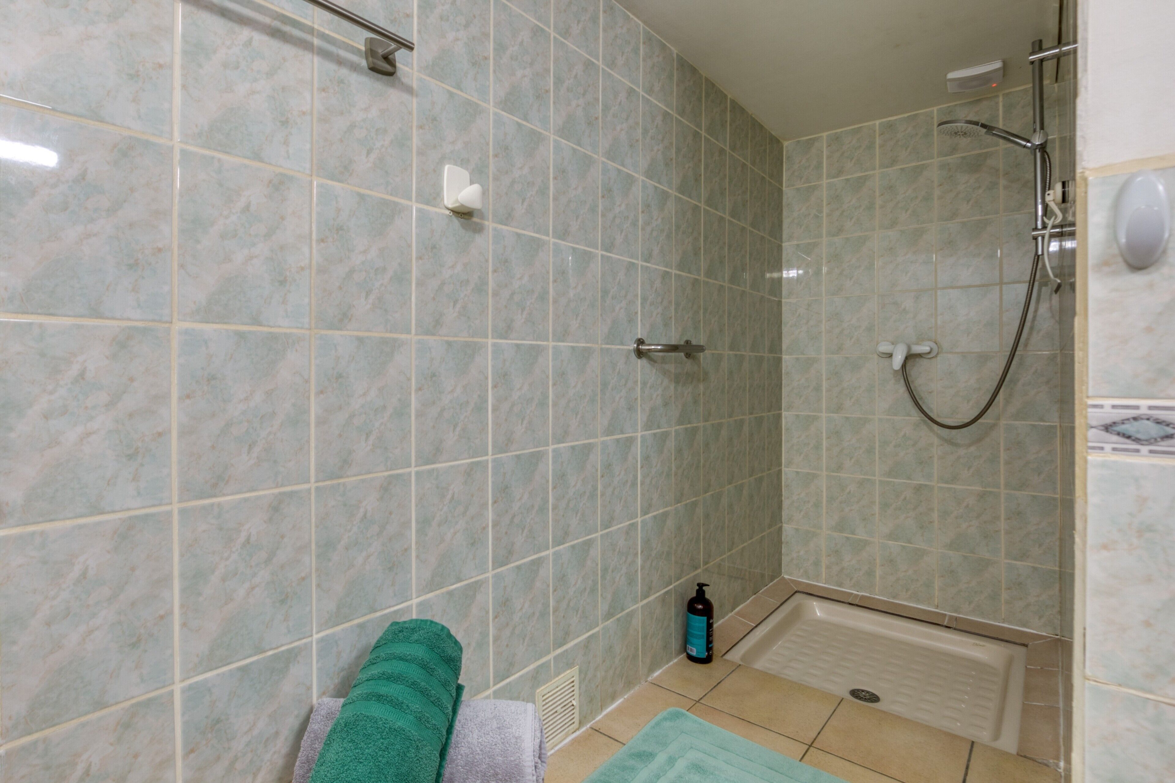 A bathroom with a shower, a towel rack, and a bottle of shampoo on the floor.