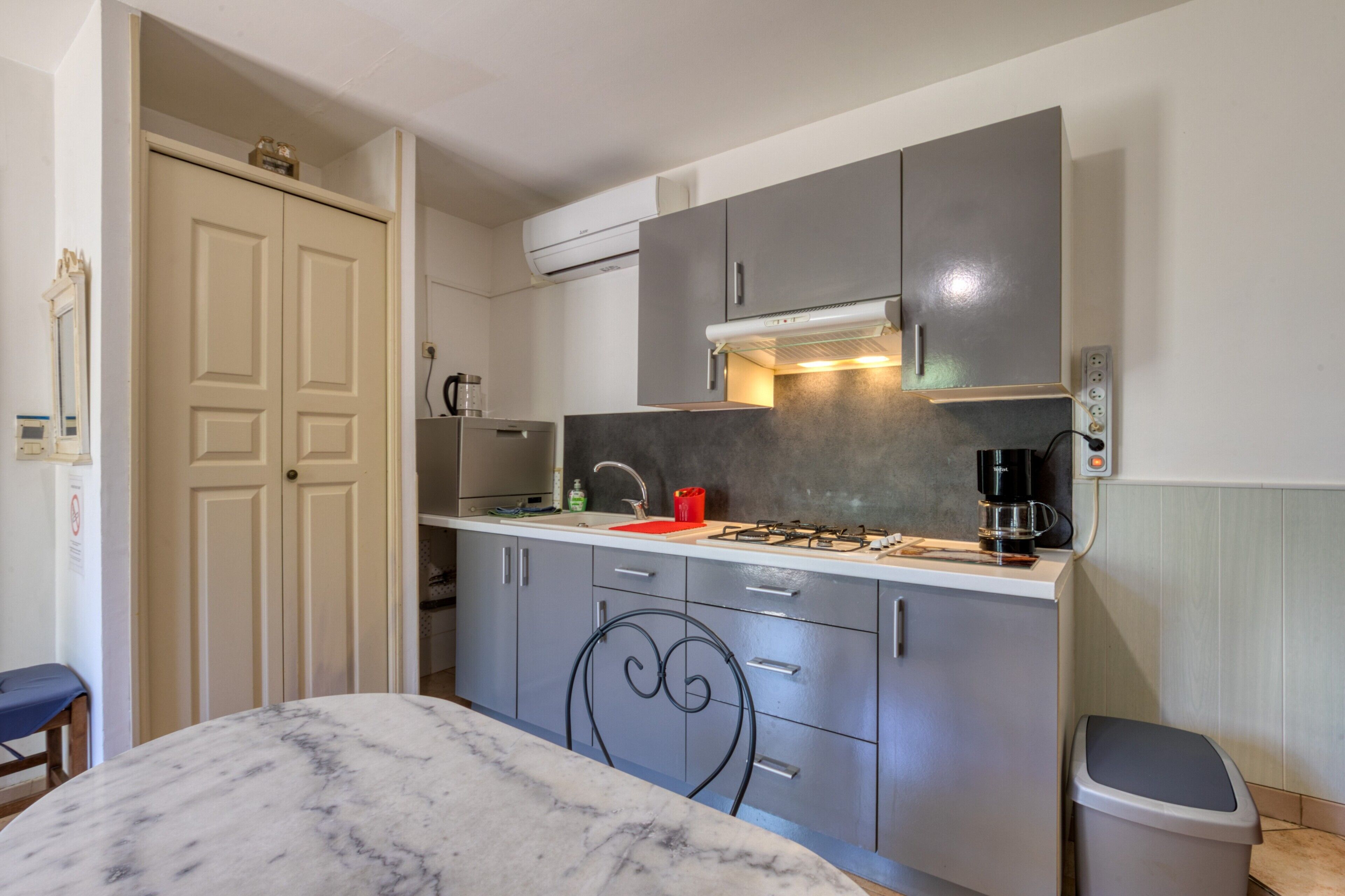 Une cuisine de taille réduite avec des meubles gris, un plan de travail en marbre et une cuisinière à gaz.