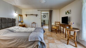 A bedroom with a bed, bedside table, lamp, TV, chair, and a small table with a vase. - Gîte l'écluse - Domaine La Noria Holiday Homes (Cazouls-lès-Béziers)