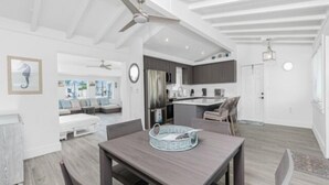 Une cuisine moderne dotée d’un îlot central, un coin repas avec une table et des chaises, et un espace de vie avec un canapé et un ventilateur de plafond.