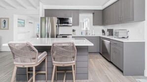 Une cuisine moderne avec des meubles gris, des appareils en acier inoxydable et un îlot central agrémenté de deux chaises en osier.