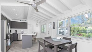 Une cuisine moderne dotée d’un îlot central, d’un coin repas avec une table et des chaises, et d’une grande fenêtre offrant une vue sur la verdure.