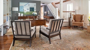 Un salon spacieux avec une table basse en bois, deux fauteuils rembourrés, une grande moquette et un tableau accroché au mur.