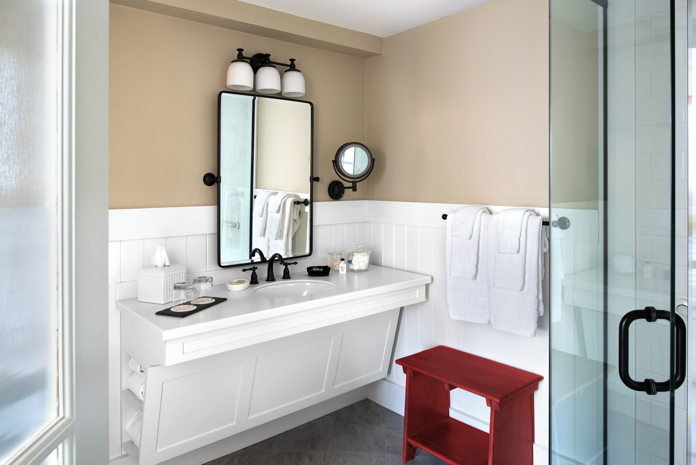 A modern bathroom with a white vanity, a glass shower enclosure, and a red bench.