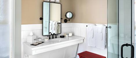 A modern bathroom with a white vanity, a glass shower enclosure, and a red bench.
