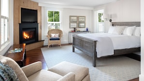 Une chambre à coucher avec un lit, une cheminée, un fauteuil, une table de chevet et des tableaux encadrés accrochés au mur.