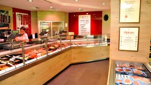 Mostrador de charcutaria com diversos tipos de carne, uma balança digital e um quadro de cardápio.