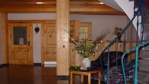 Interior em madeira com escada, porta com janela e mesa com um vaso de flores.