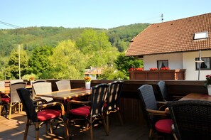 Een terras met rieten stoelen en rode kussens, een houten tafel en uitzicht op een heuvel.