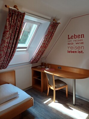 Een kamer met een bed, een bureau, een stoel, een raam met gordijnen en een muur met een motiverende quote.