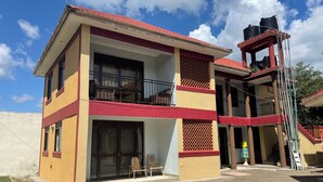 Un bâtiment à deux étages, doté d’un toit rouge, d’un balcon avec des meubles en osier et d’un réservoir d’eau sur le toit.