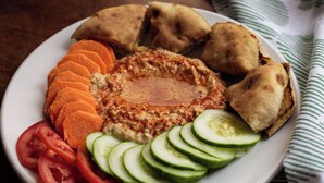 Une assiette de houmous, de concombres en tranches, de tomates et de pain pita.