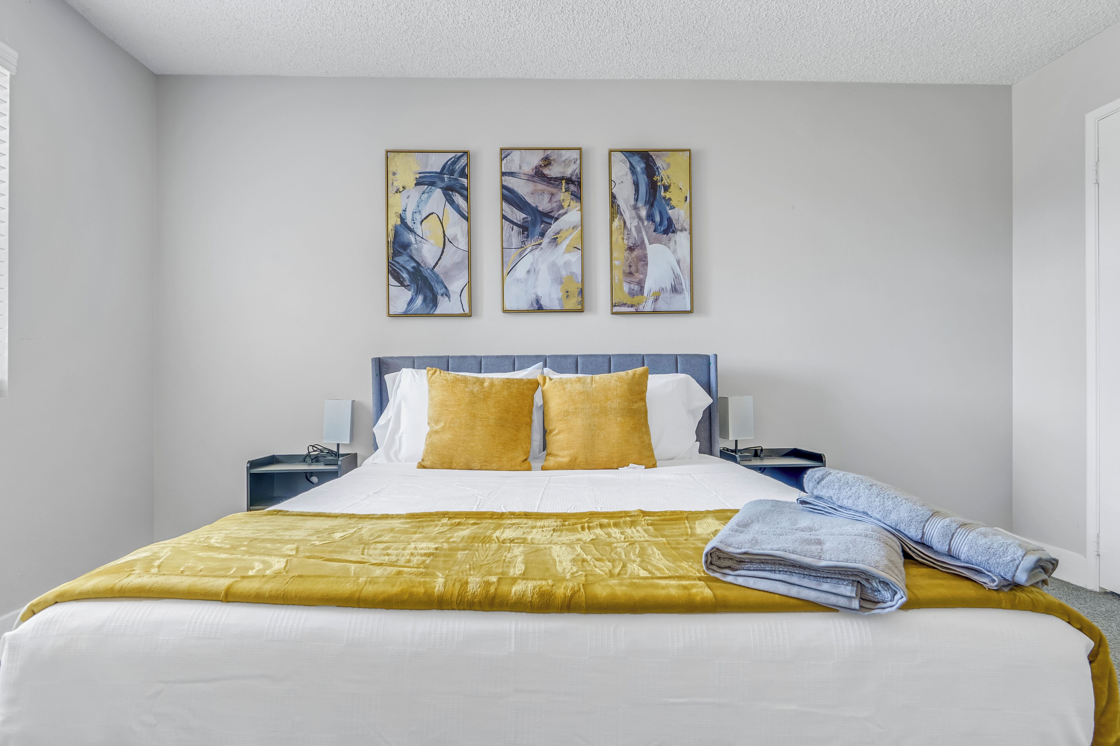 A hotel room with a large bed, a nightstand, a lamp, and abstract wall art.