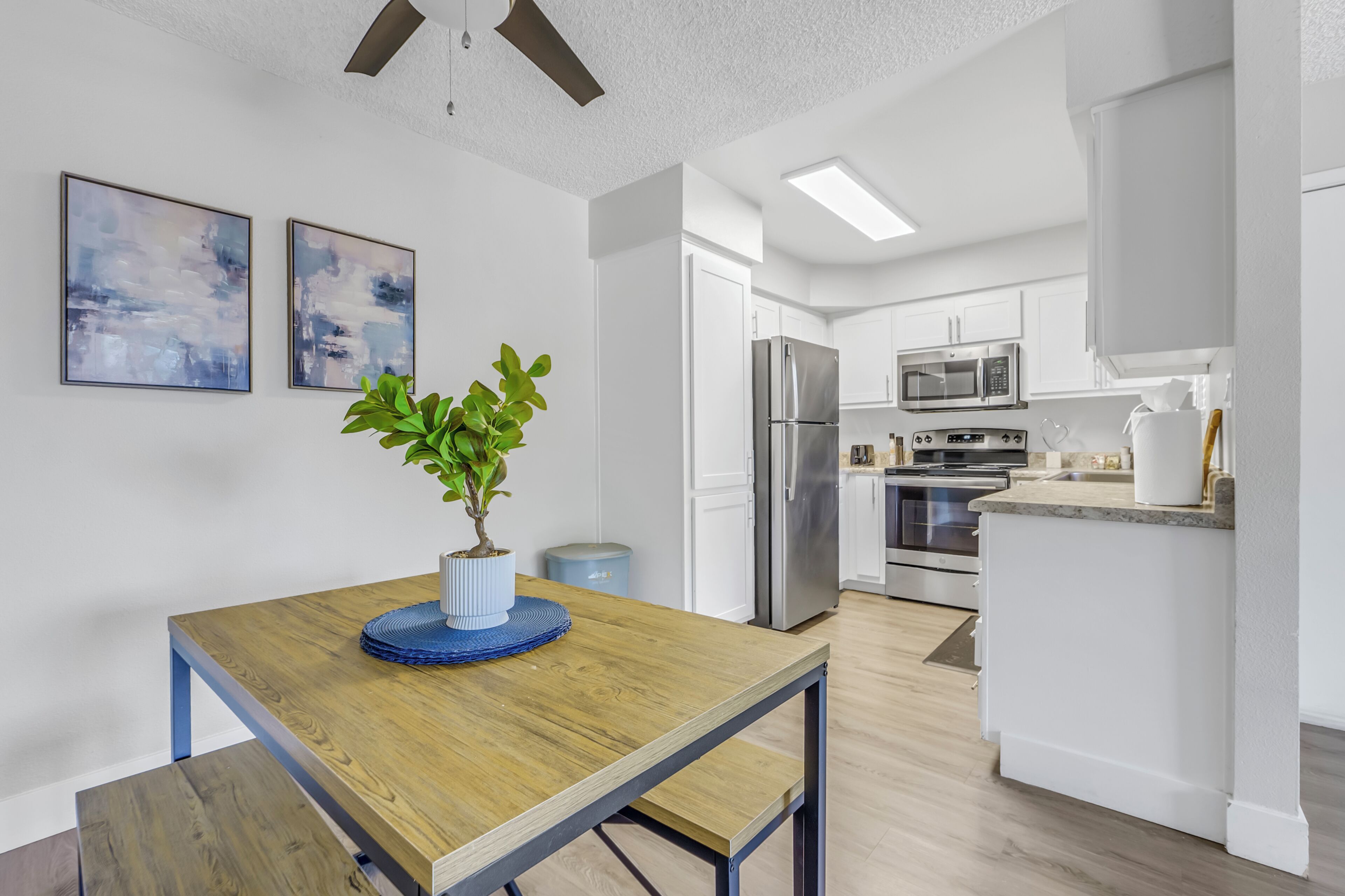 A modern kitchen with white cabinets, stainless steel appliances, and a wooden dining table with a potted plant.