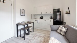 A compact kitchen with white cabinets, a black refrigerator, and a dining area with a table and bench. - Modern City Apartment in London (London)