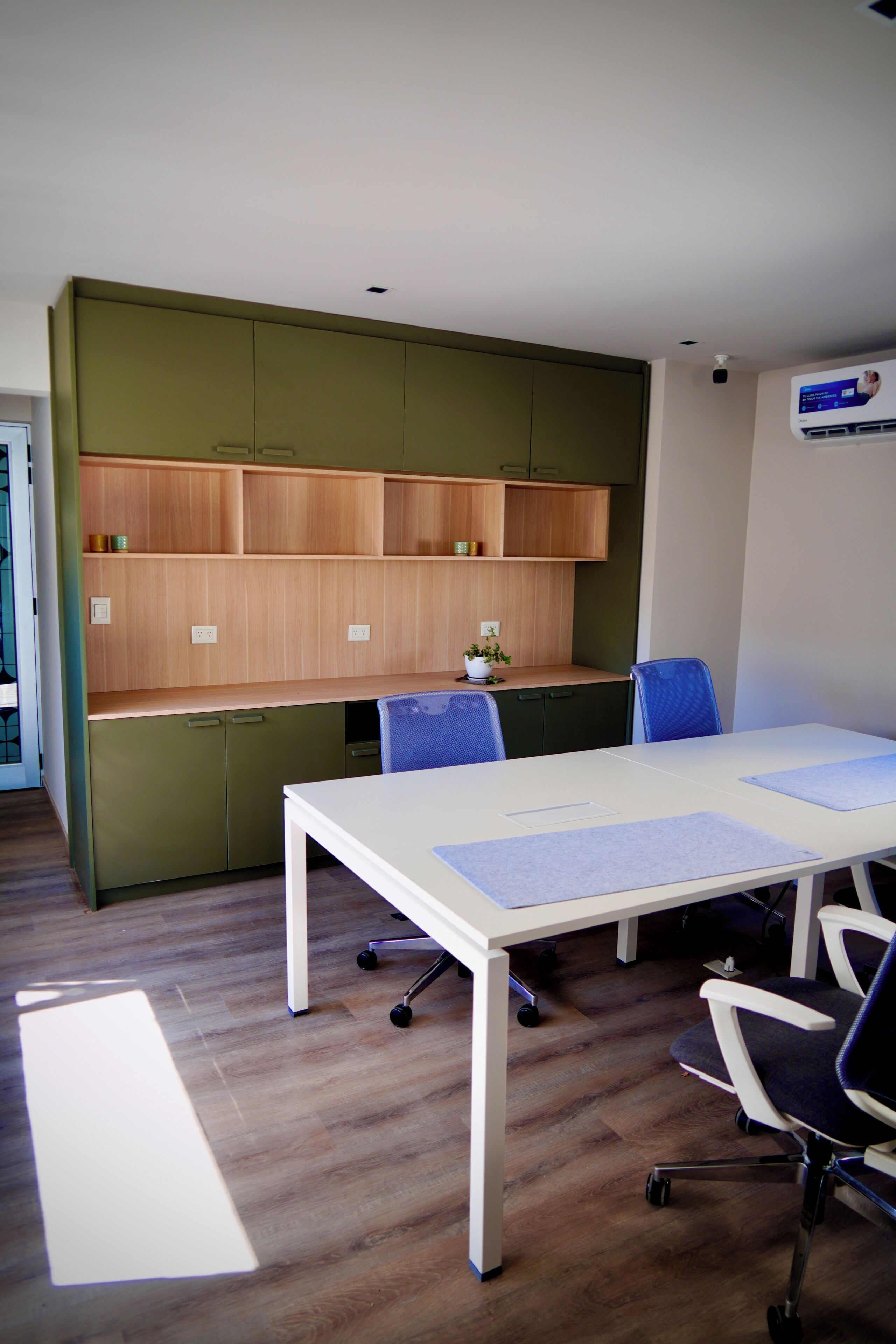 A modern meeting room with a white table, blue chairs, and a green cabinet with wooden shelves.