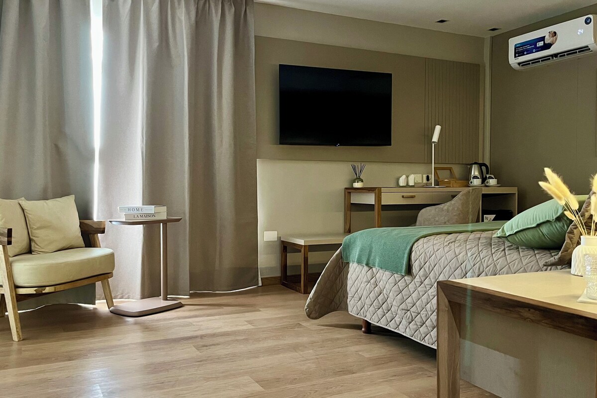 Ein modernes Hotelzimmer mit Bett, Schreibtisch, Sessel, Fernseher und Klimaanlage.