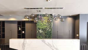 A reception desk with a marble top, a green vertical garden, and a ceiling with hanging spherical lights. - Empire Hotel Buenos Aires (Buenos Aires)