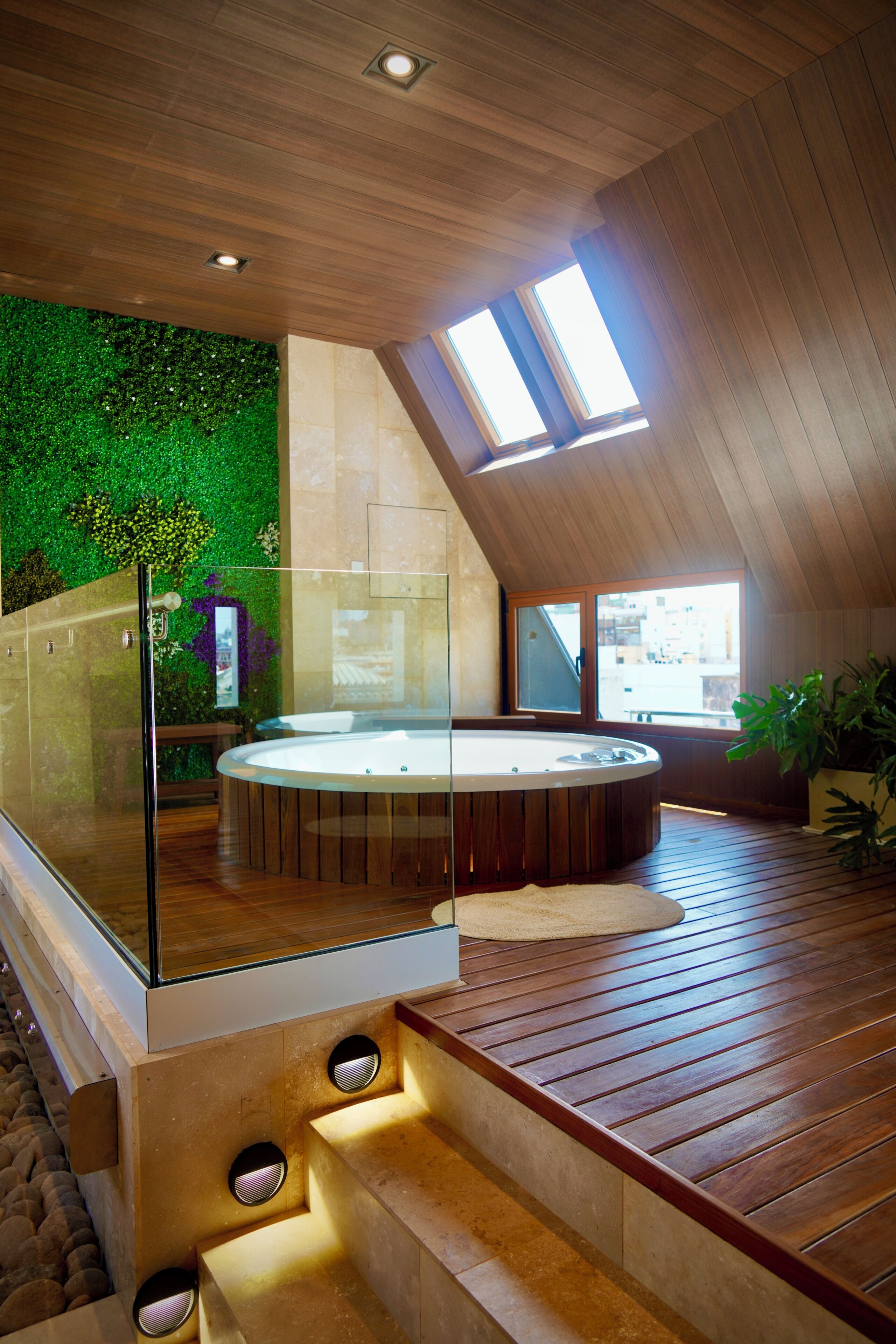 Un interior moderno con un jacuzzi de vidrio, suelo de madera y una pared verde con follaje.