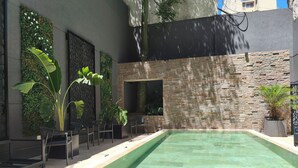A modern outdoor pool area with a stone wall, seating, and lush greenery. - Empire Hotel Buenos Aires (Buenos Aires)