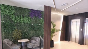 A lobby with a green wall, two grey armchairs, a small table, and a potted plant. - Empire Hotel Buenos Aires (Buenos Aires)