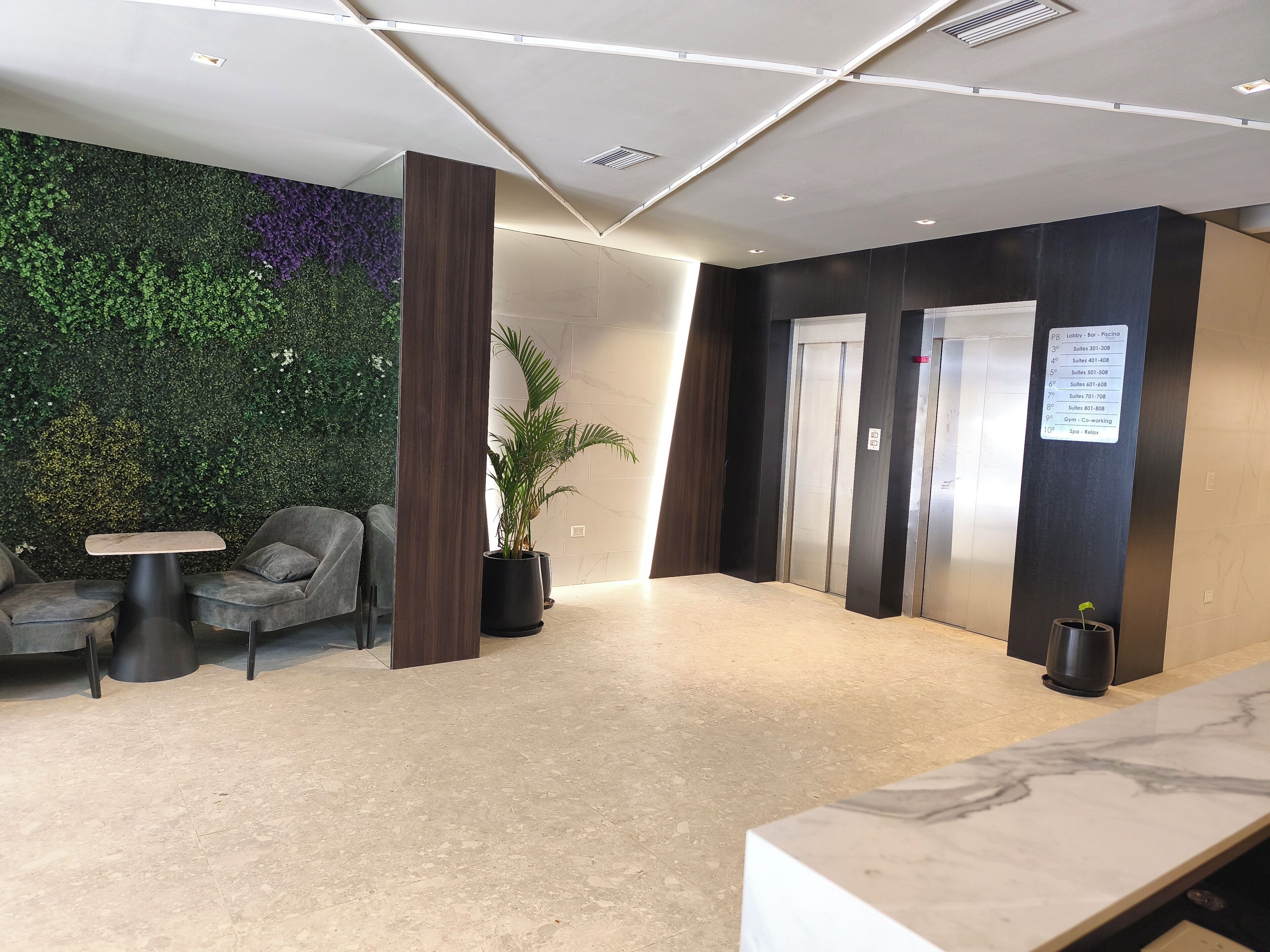 A modern lobby with a green wall, two grey sofas, a small table, and a reception desk.