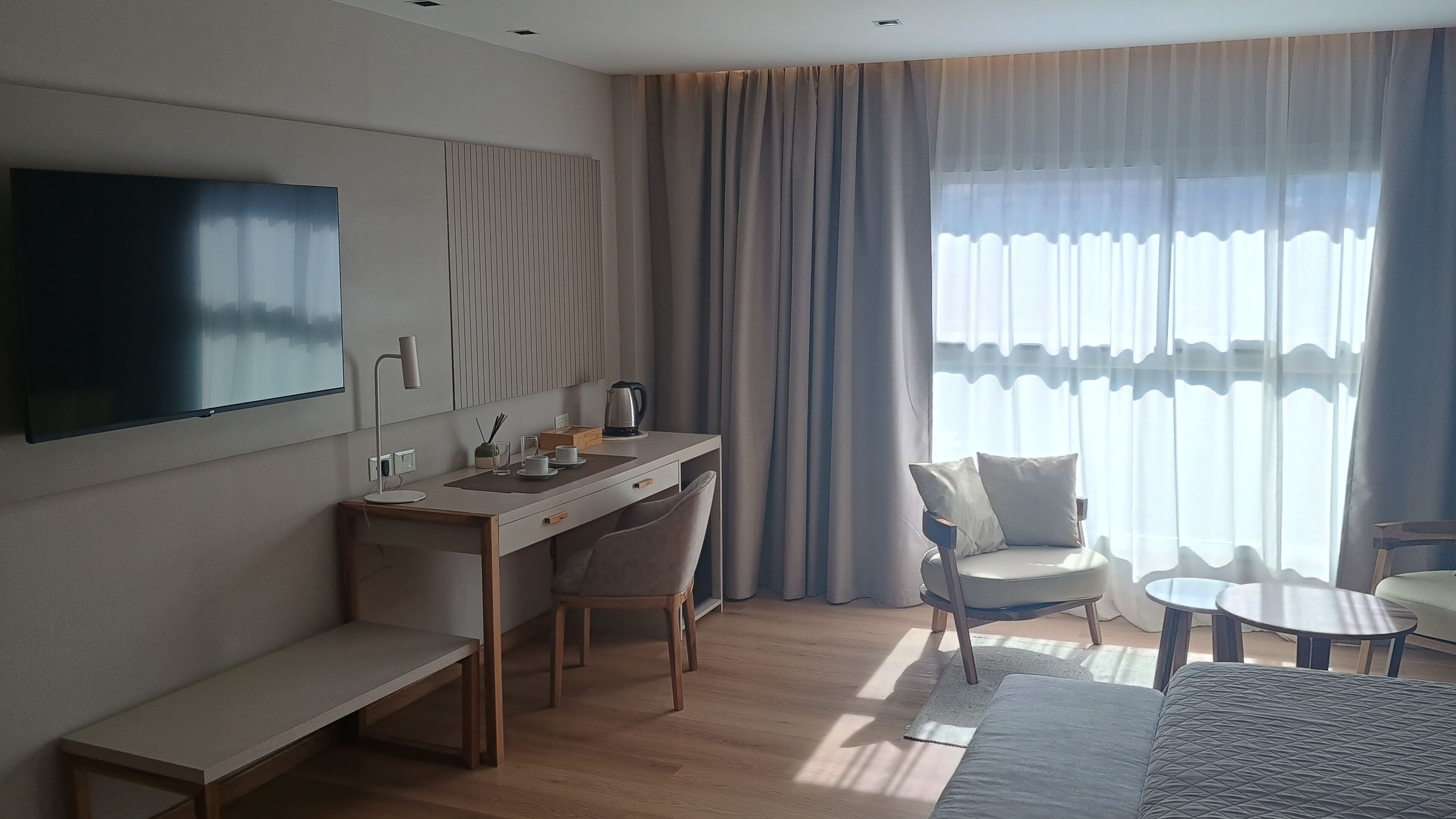 A modern hotel room with a flat-screen TV, a desk with chairs, a sofa, and a coffee table.