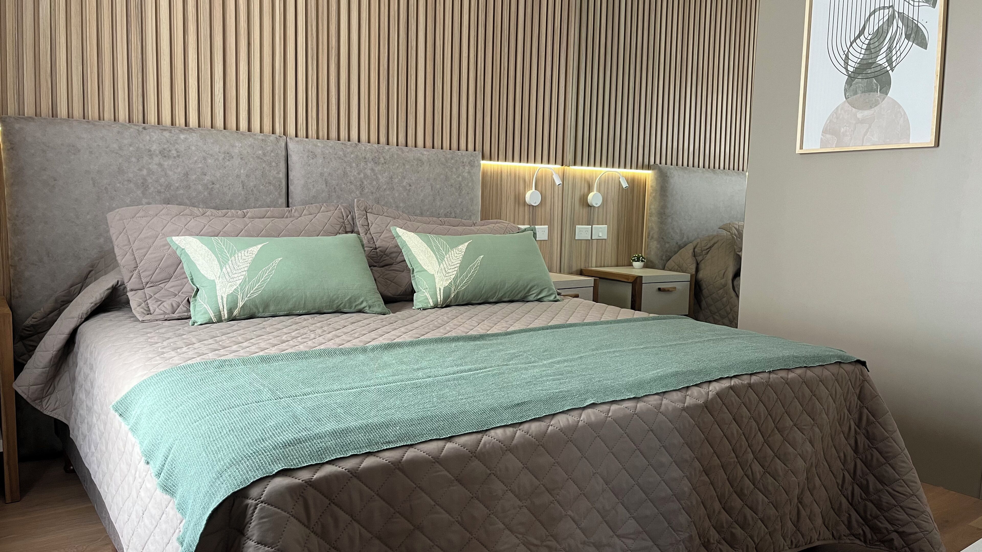 A modern bedroom with a large bed, two nightstands, a wall-mounted lamp, and a framed picture.