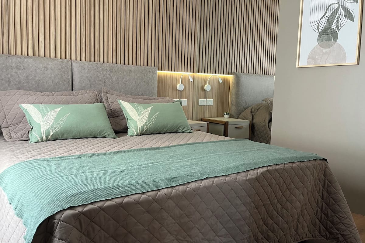 A modern bedroom with a large bed, two nightstands, a wall-mounted lamp, and a framed picture.