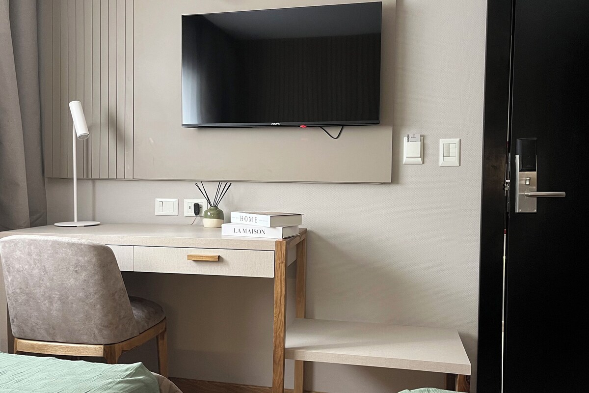 A hotel room with a desk, chair, and a television mounted on the wall.