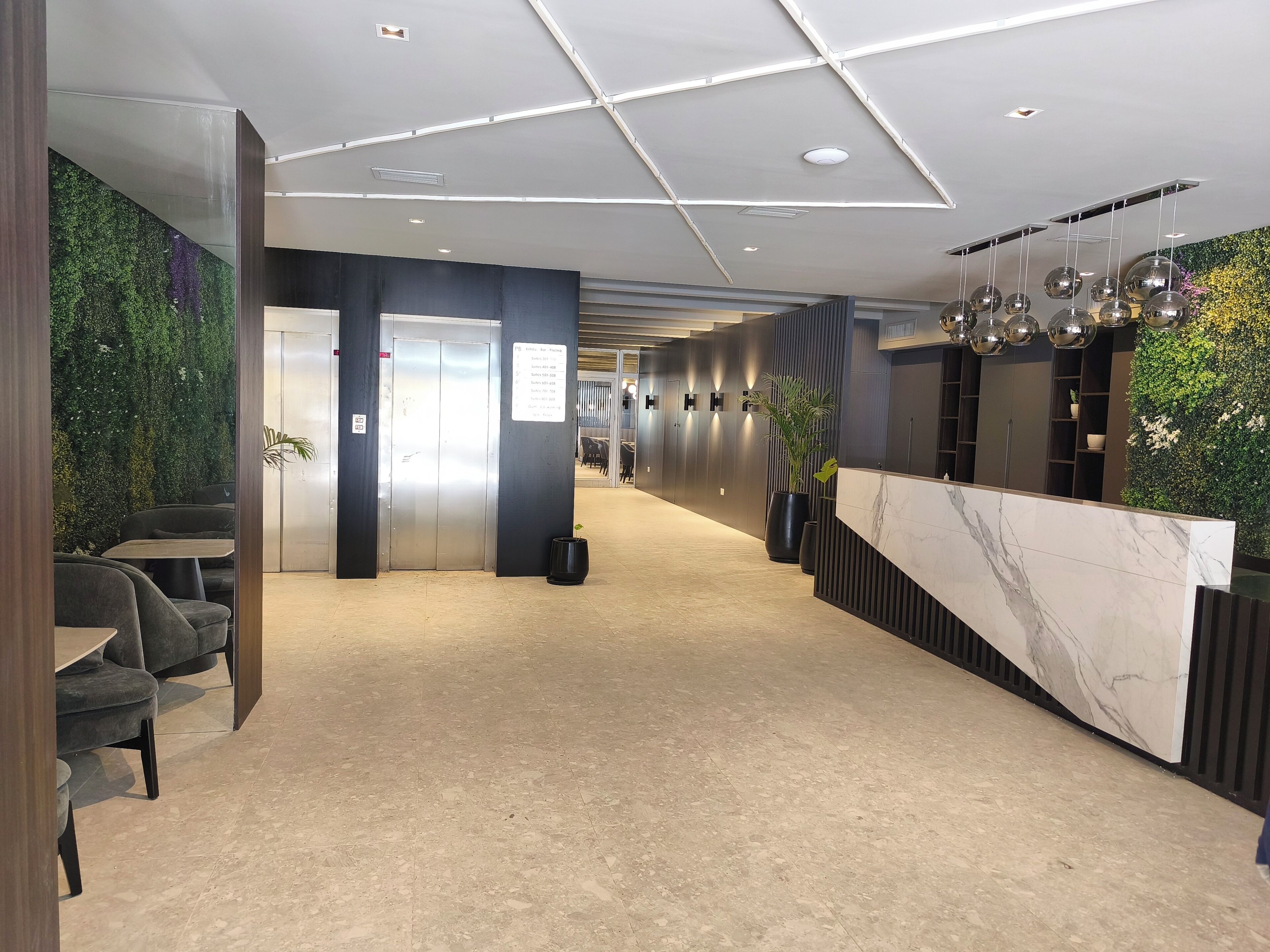 Un hall d’hôtel moderne avec un comptoir d’accueil, un espace salon et un mur végétal.