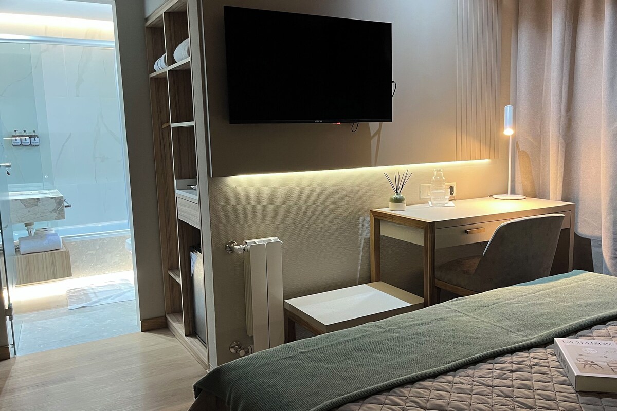 Ein Hotelzimmer mit Bett, Schreibtisch, Stuhl, Fernseher und einem Badezimmer mit Dusche und Toilette.