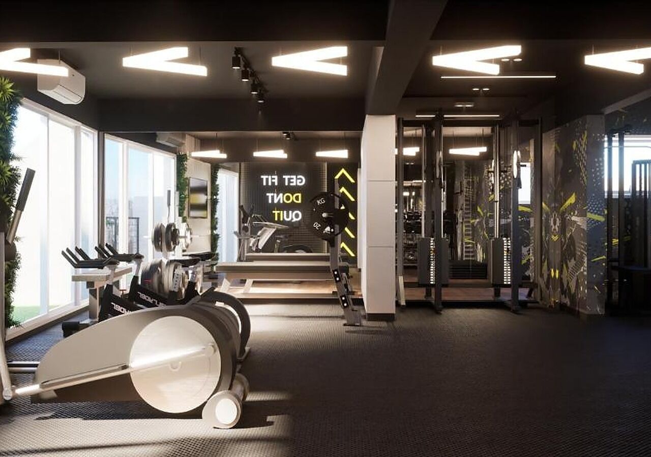 Un gimnasio con equipo de ejercicio, un espejo grande y una frase motivacional.