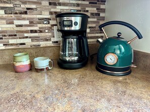 A kitchen counter with a coffee maker, a kettle, and two mugs.
