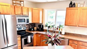 A modern kitchen with wooden cabinets, stainless steel appliances, a granite countertop, and a central island with stools. - Stay between Glacier and Whitefish-cozy stylish (Columbia Falls)
