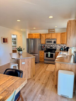 A modern kitchen with wooden cabinets, stainless steel appliances, and a built-in oven. - Stay between Glacier and Whitefish-cozy stylish (Columbia Falls)
