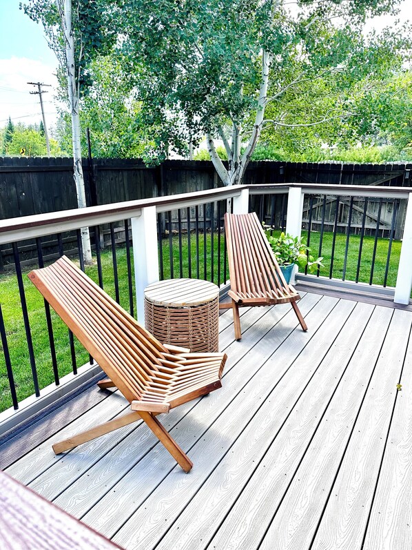 A wooden deck with two lounge chairs and a round table.