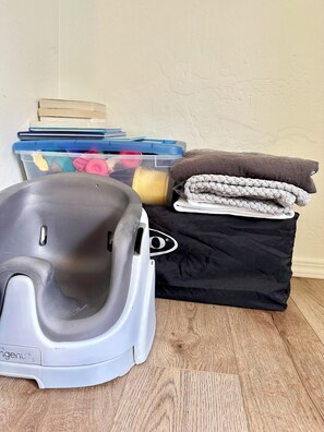 A gray mobility aid, a black storage bin with a cushion, and a stack of books on a wooden floor against a textured wall.