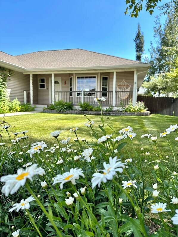 A house with a front porch, a lawn, and white flowers in the foreground.