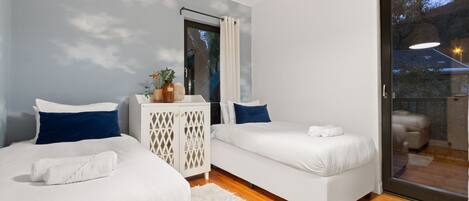 A modern bedroom with two single beds, a white wardrobe, and a large sliding glass door leading to an outdoor area.