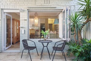 A patio with two chairs and a table, a wooden cabinet, and a hanging light fixture. - Mimosa Court (Cape Town)